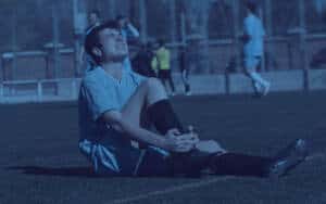 sports injury - kids soccer injury - teen in soccer uniform clutching ankle